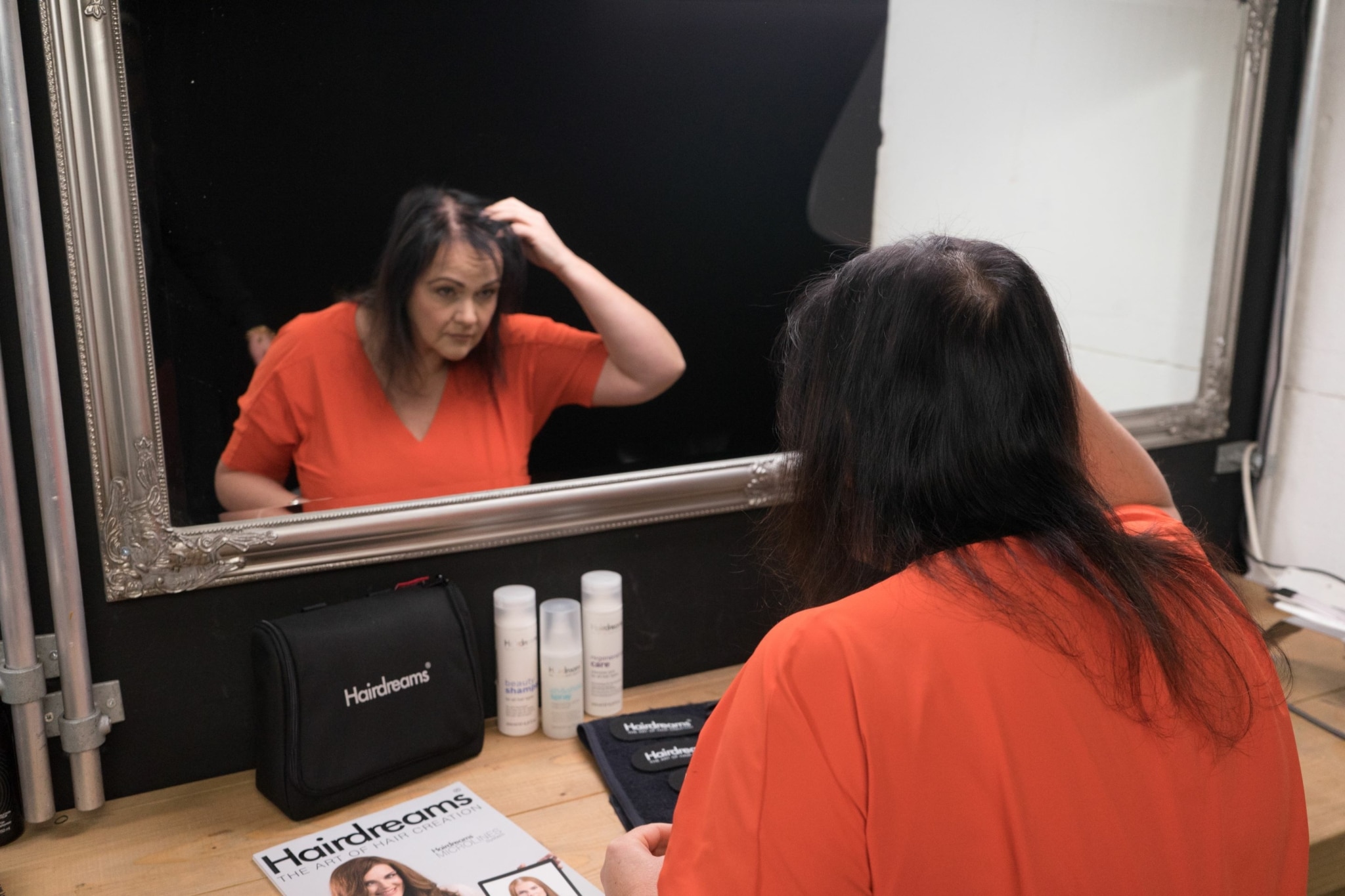 Frau mit ausgedünntem schwarzen Haar betrachtet sich im Spiegel