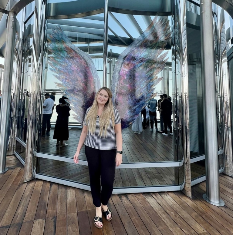 Hairdreams-Mitarbeiterin posiert vor bunten Engelsflügeln in Dubai