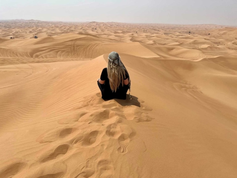 Hairdreams-Mitarbeiterin sitzt in der Wüste Dubais und blickt in die unendliche Weite.