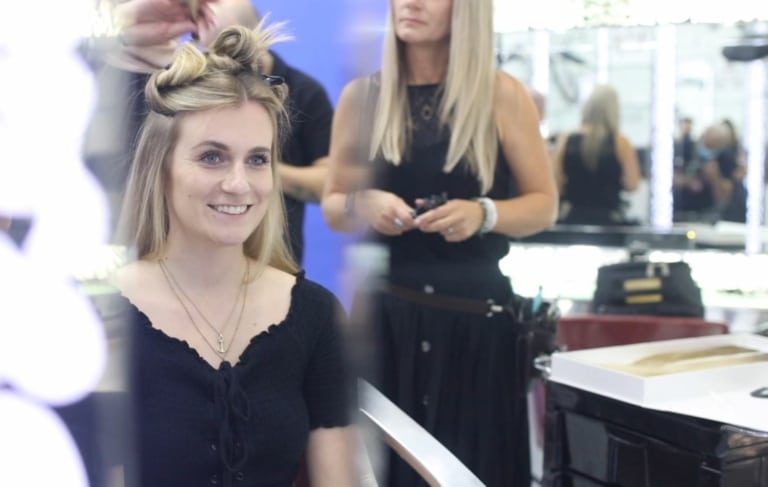 Eine junge Frau sitzt im Friseursalon und freut sich auf ihre Haarverlängerung