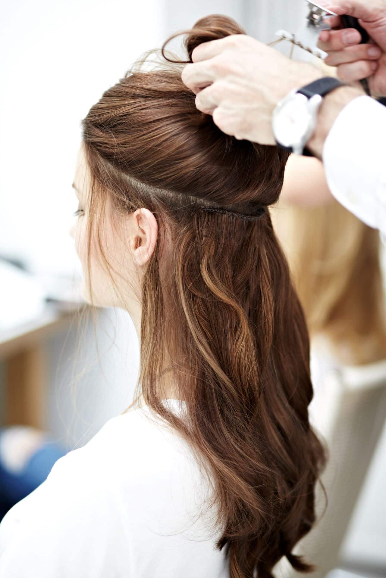 Peluquera levanta el cabello superior de una clienta, dejando al descubierto la trama de cabello natural Hairdreams integrada.
