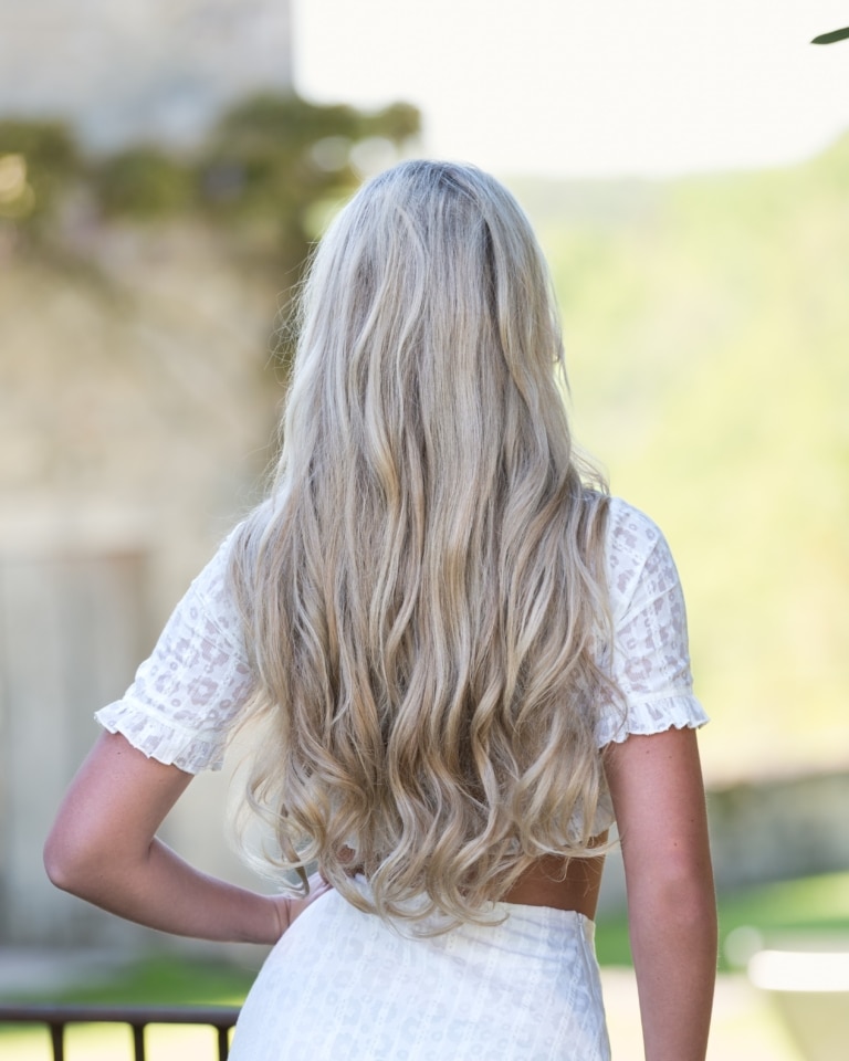 Donna con capelli lunghi biondi e un'estensione con trame di capelli umani da dietro.