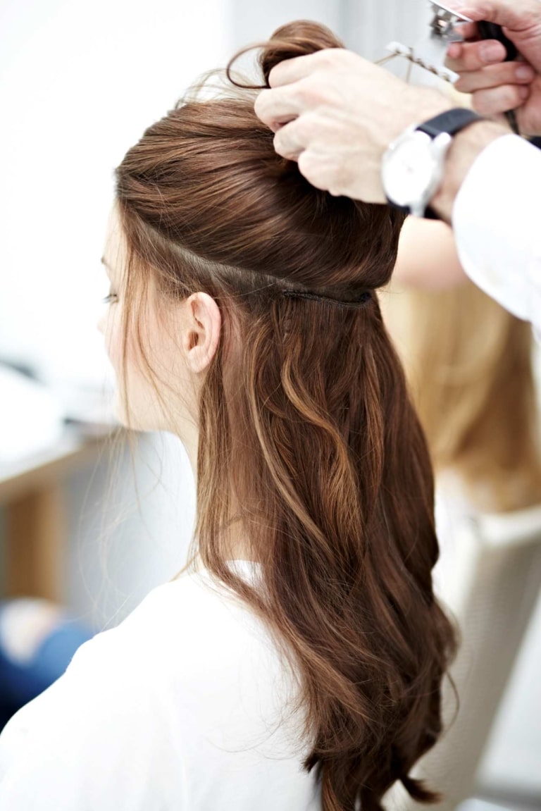 Friseur hebt die Haare einer Kundin hoch, um die darunter angebrachten Hairdreams Haartressen zu zeigen.