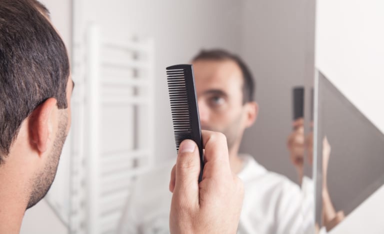 Man holding a comb in his hand and standing in front of a mirror